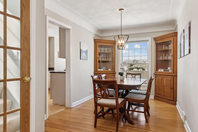 dining space featuring an inviting chandelier, baseboards, light wood-type flooring, and a textured ceiling