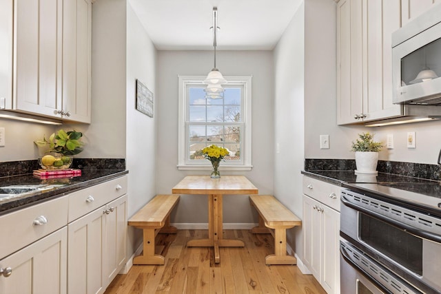 kitchen with baseboards, range with two ovens, hanging light fixtures, light wood-type flooring, and breakfast area