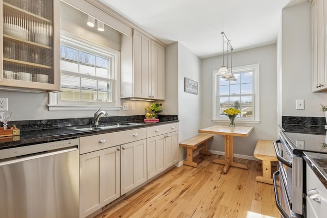 kitchen featuring decorative light fixtures, dark stone counters, light wood-type flooring, appliances with stainless steel finishes, and a sink