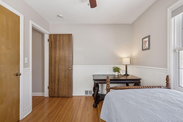 bedroom with a ceiling fan, wood finished floors, visible vents, and wainscoting