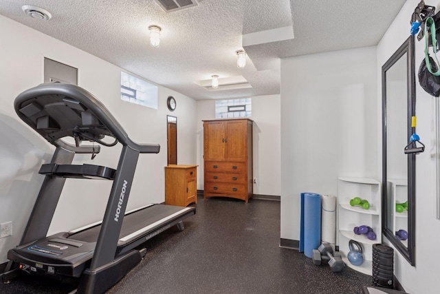 exercise room featuring visible vents, a textured ceiling, and baseboards