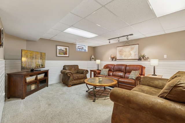 living area featuring a drop ceiling, a wainscoted wall, and carpet