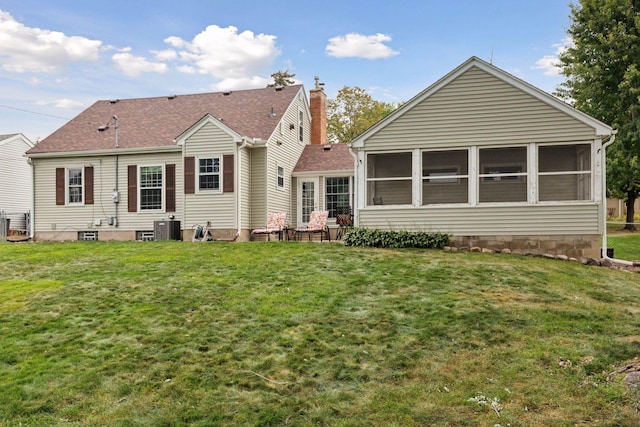 rear view of house featuring cooling unit, a sunroom, a shingled roof, a chimney, and a lawn