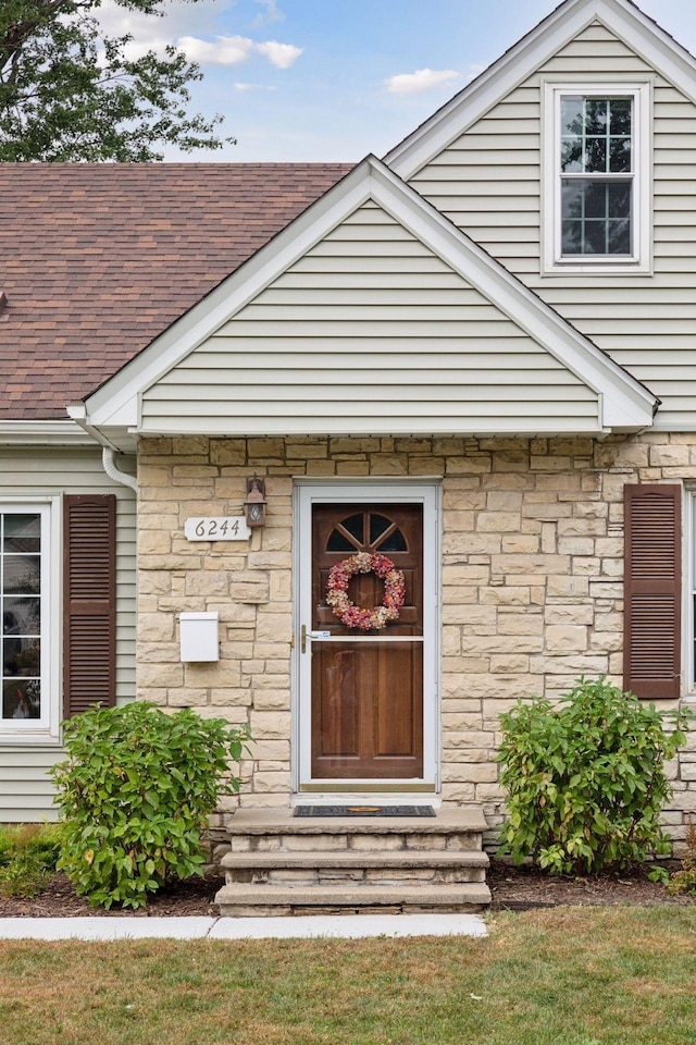 view of exterior entry with stone siding and roof with shingles