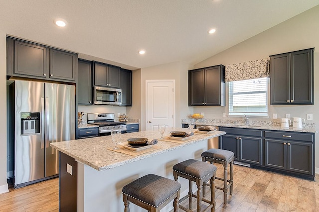 kitchen featuring lofted ceiling, a breakfast bar area, a sink, appliances with stainless steel finishes, and a center island