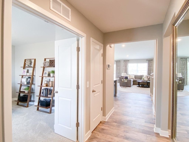 corridor featuring light wood finished floors, baseboards, and visible vents