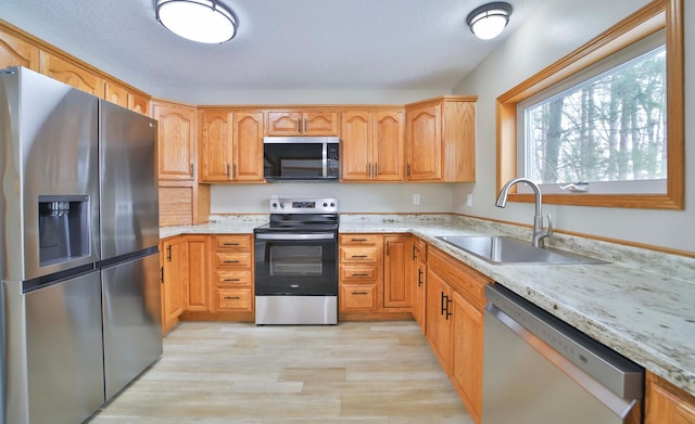 kitchen featuring light stone countertops, light wood-style floors, a textured ceiling, stainless steel appliances, and a sink