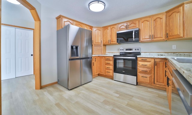 kitchen featuring light stone countertops, light wood-style flooring, appliances with stainless steel finishes, arched walkways, and a sink