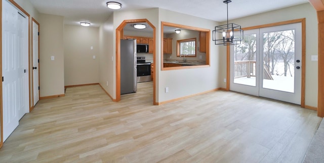 interior space with light wood-style flooring, a sink, decorative light fixtures, appliances with stainless steel finishes, and baseboards