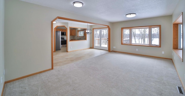 unfurnished living room featuring visible vents, light colored carpet, a textured ceiling, and baseboards