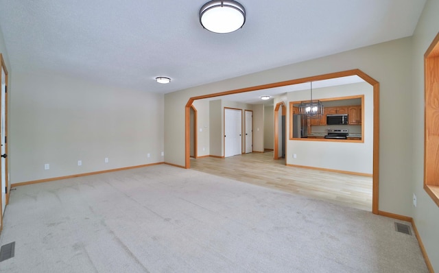 unfurnished living room with baseboards, visible vents, arched walkways, and light carpet