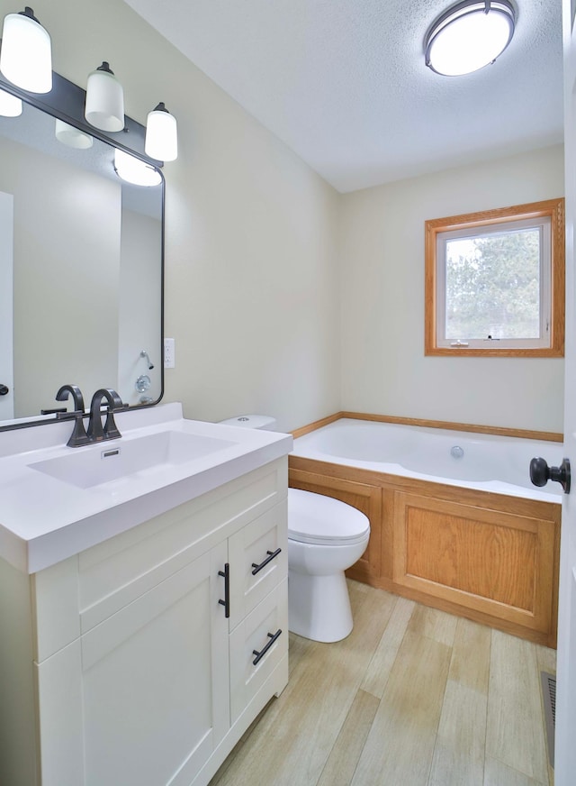 bathroom featuring toilet, vanity, a garden tub, wood finished floors, and a textured ceiling