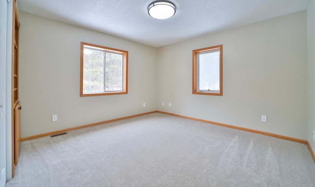 empty room featuring light carpet, baseboards, visible vents, and a textured ceiling