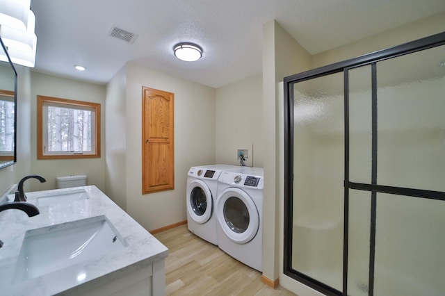 laundry room with a sink, visible vents, light wood-style floors, and washing machine and dryer