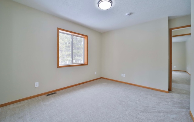 empty room featuring visible vents, light colored carpet, a textured ceiling, and baseboards