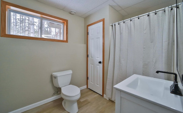 full bath featuring wood finished floors, baseboards, a drop ceiling, a sink, and toilet