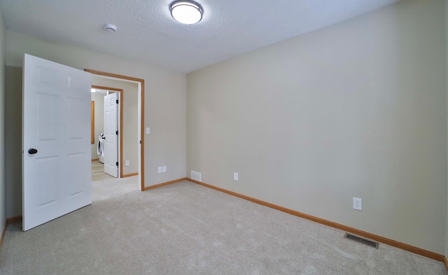 spare room featuring visible vents, washer and dryer, a textured ceiling, baseboards, and light colored carpet