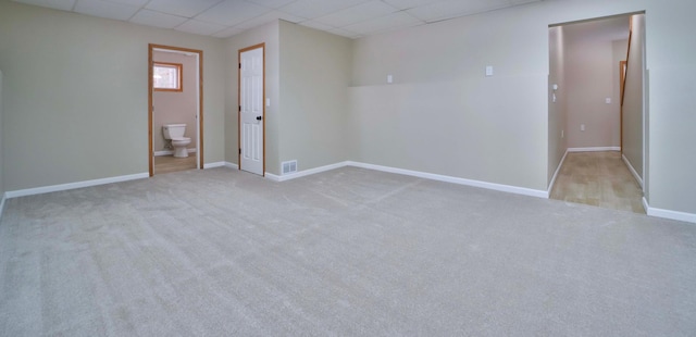 carpeted spare room with a paneled ceiling, visible vents, and baseboards