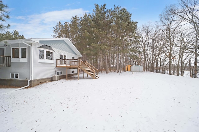 snow covered back of property with a storage unit, stairway, an outbuilding, and a wooden deck