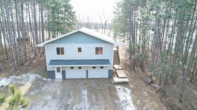 view of side of home featuring stairs, an attached garage, dirt driveway, and a shingled roof