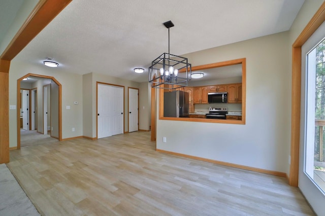 1505 Harrison Dr SW, Brainerd, MN 56401 - unfurnished living room with light wood-type flooring, a chandelier, arched walkways, baseboards, and a textured ceiling