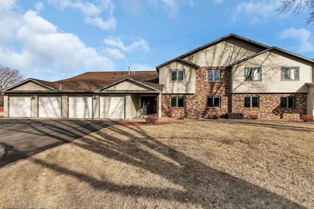 view of front of house with brick siding, a front lawn, and community garages