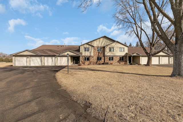 view of front of house with stone siding, a front lawn, an attached garage, and driveway