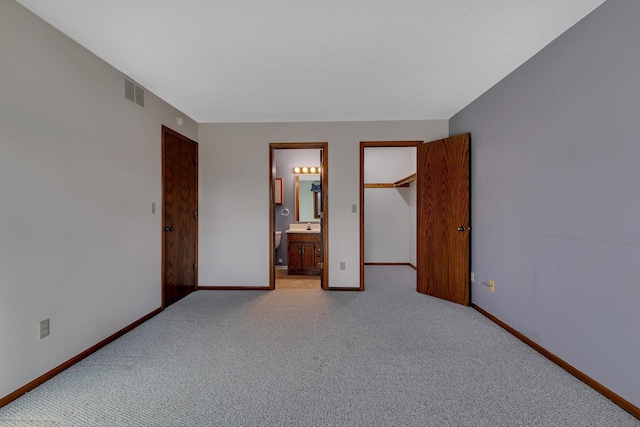 unfurnished bedroom featuring a closet, light colored carpet, visible vents, ensuite bathroom, and baseboards