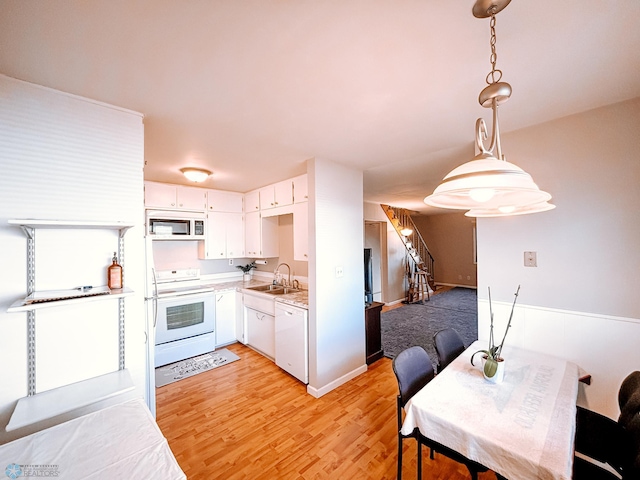 kitchen with light countertops, light wood-style flooring, white cabinetry, a sink, and white appliances