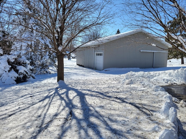 view of snowy exterior featuring a garage, an outdoor structure, and a pole building