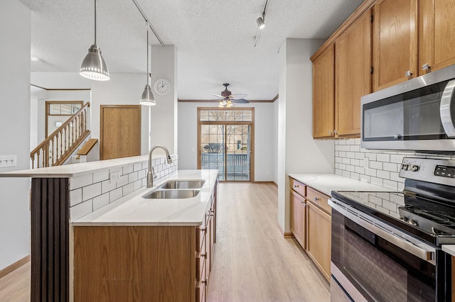 kitchen featuring light wood finished floors, backsplash, appliances with stainless steel finishes, a sink, and a textured ceiling