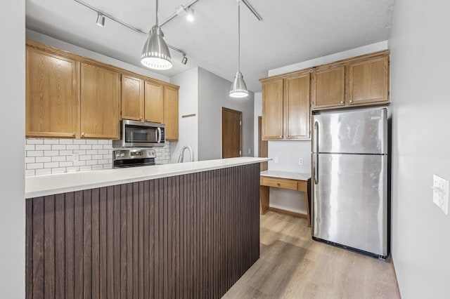 kitchen featuring appliances with stainless steel finishes, a peninsula, light countertops, light wood-style floors, and backsplash