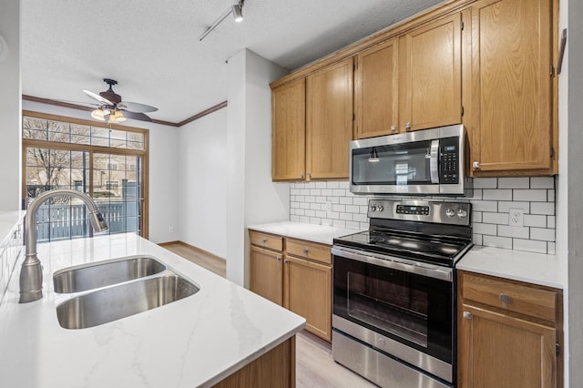 kitchen with a sink, stainless steel appliances, crown molding, a textured ceiling, and backsplash