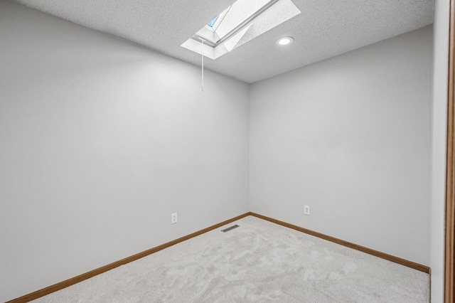 spare room with a skylight, baseboards, visible vents, carpet, and a textured ceiling