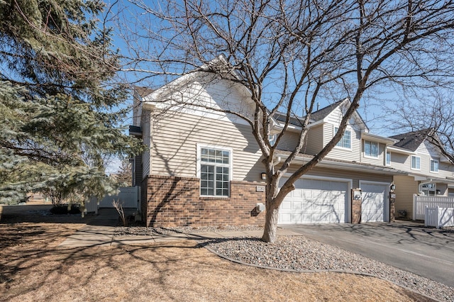 view of property exterior featuring a garage, driveway, fence, and brick siding