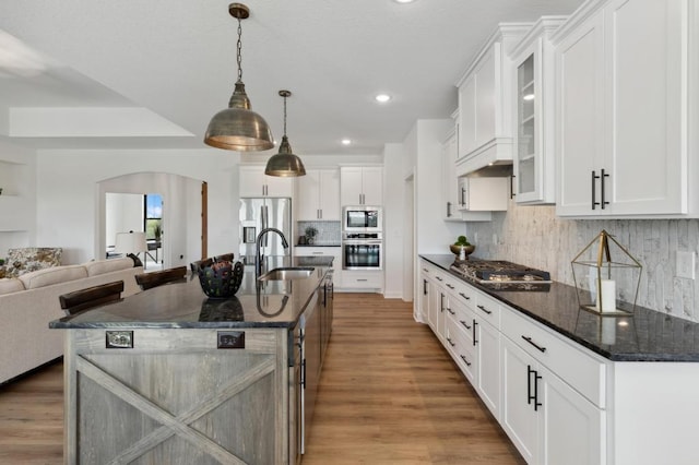 kitchen with glass insert cabinets, open floor plan, appliances with stainless steel finishes, arched walkways, and a sink