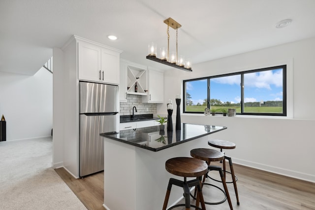 kitchen with a breakfast bar area, decorative backsplash, freestanding refrigerator, white cabinets, and a sink