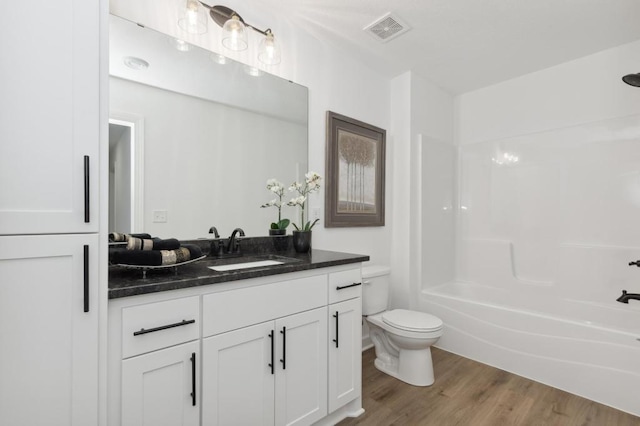 bathroom featuring visible vents, toilet, vanity, wood finished floors, and washtub / shower combination