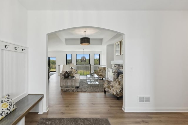 entrance foyer featuring arched walkways, wood finished floors, a fireplace, a raised ceiling, and baseboards