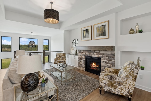 living area featuring a raised ceiling, a fireplace, wood finished floors, and a chandelier