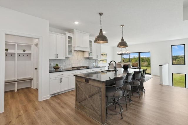 kitchen featuring a sink, stainless steel gas stovetop, light wood-type flooring, an island with sink, and backsplash