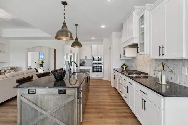 kitchen featuring appliances with stainless steel finishes, a sink, arched walkways, glass insert cabinets, and open floor plan