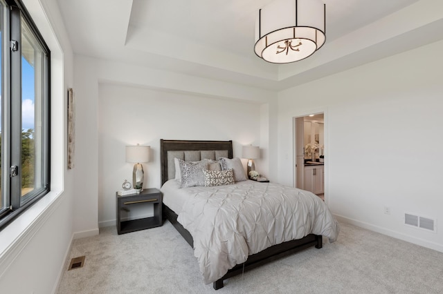 carpeted bedroom featuring baseboards, a tray ceiling, and ensuite bathroom