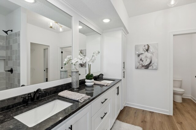 full bathroom featuring wood finished floors, double vanity, toilet, and tiled shower