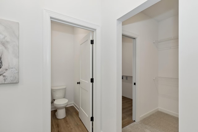 bathroom with toilet, a spacious closet, baseboards, and wood finished floors