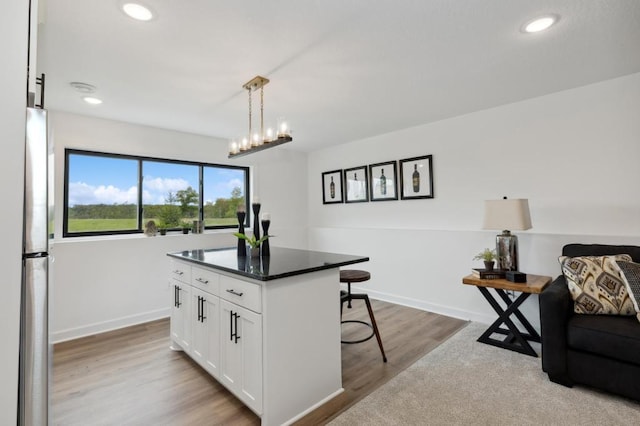 kitchen featuring a breakfast bar area, white cabinetry, a center island, dark countertops, and freestanding refrigerator