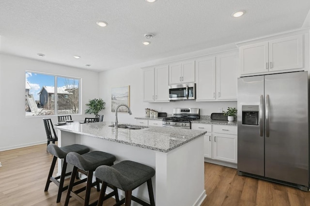 kitchen with light wood-style flooring, a sink, light stone counters, white cabinetry, and stainless steel appliances