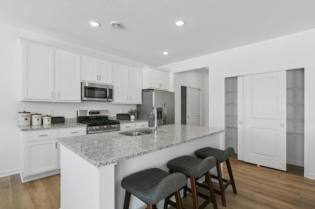 kitchen featuring a kitchen breakfast bar, wood finished floors, white cabinets, stainless steel appliances, and a sink