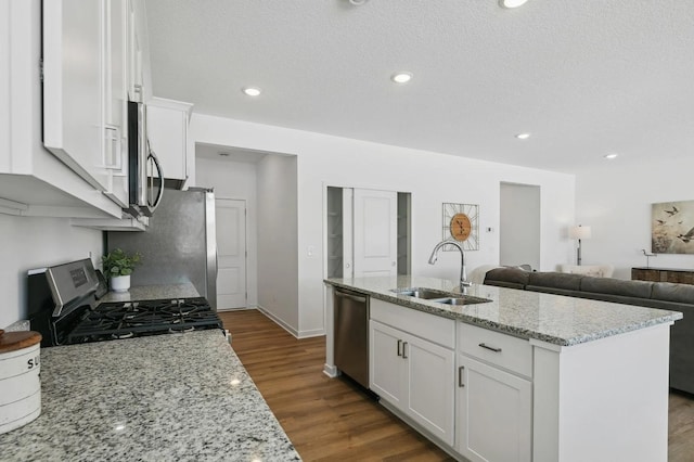 kitchen featuring dark wood finished floors, an island with sink, a sink, appliances with stainless steel finishes, and white cabinetry