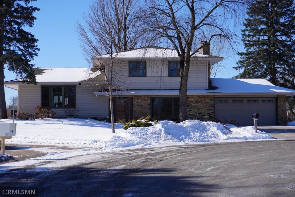 view of front facade featuring brick siding, driveway, a chimney, and an attached garage